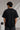 Man wearing a black BROKEN CODE oversized t-shirt with a glitch art graphic of eyes and text. Features a chain necklace and dark wash jeans. Model is posed against a studio backdrop.