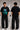 Man wearing a black BROKEN CODE oversized t-shirt with a glitch art graphic of eyes and text. Features a chain necklace and dark wash jeans. Model is posed against a studio backdrop.