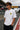 Model wearing white POPCASE Charles Leclerc Scuderia Ferrari oversized t shirt with prancing horse shield badge at F1 circuit pitlane