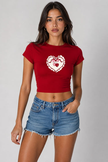 Model wearing a red CROPTOP Cherry crop top with a cute cherry and bow graphic, paired with denim shorts. The top has a flattering cropped fit. - red