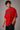 Male model wearing a red oversized t-shirt with 'Believe' printed in navy blue and white collegiate-style lettering.