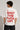 Person wearing a white t-shirt with red text on the back, standing against a plain background