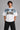 Model wearing a white DIMENSION oversized t-shirt with a black and blue graphic print and a silver chain necklace. - white