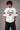 Back view of a man wearing a white LA 32 Drive oversized t-shirt with black text graphic. Model wears black cargo pants. - white