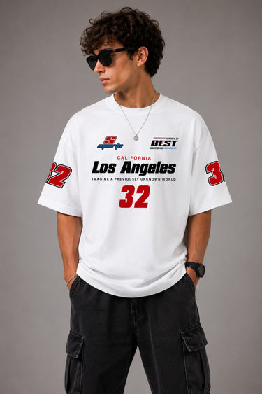 Back view of a man wearing a white LA 32 Drive oversized t-shirt with black text graphic. Model wears black cargo pants. - white