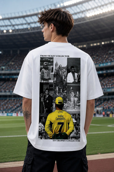 A man standing on a sports field in front of a stadium, wearing a white t-shirt with a large black-and-yellow graphic print on the back. The print features text reading 'FROM TICKET COLLECTOR TO TROPHY COLLECTOR' and a collage of cricket player images, including a prominent yellow jersey.
