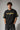 Model wearing an anthracite black Mbappe oversized t-shirt with gold "MBAPPE" graphic and signature, Real Madrid and number 7 logos on sleeves.