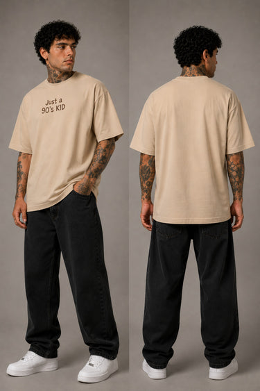 Model wearing a red oversized t-shirt with 'Just a 90's Kid' graphic. The tee has a relaxed fit, paired with black jeans and white sneakers, embodying a retro streetwear style. - beige