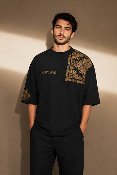 Back view of a person wearing a black ART ON OVERSIZED TSHIRT with gold embroidered detail on the left sleeve. Shows the oversized fit and premium streetwear aesthetic. - black