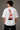 Man wearing white F1 Official oversized t-shirt with red F1 logo, black wide-leg jeans, and white sneakers, sitting on a black leather couch. - white