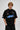 Model wearing a black Fast Feels Forever oversized t-shirt with graphic prints, sitting on a leather couch. - black