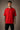 Man wearing a red FCB Messi fan oversized t-shirt, black pants, and white sneakers, sitting on a brown couch. - red