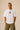 Man wearing a white oversized Real Madrid t-shirt with a circular club crest logo, paired with olive green pants and black sneakers, posing casually with hands in pockets. - white