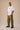 Man wearing a white oversized Real Madrid t-shirt with a circular club crest logo, paired with olive green pants and black sneakers, posing casually with hands in pockets.