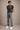 Man wearing a dark gray t-shirt, jeans, and white sneakers against a beige background