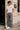 Man wearing a white t-shirt and gray jeans standing against a building wall.