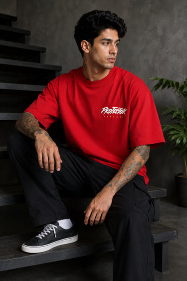 Red oversized t-shirt with 'PROJECTOR HANUMANJI' graphic design of a warrior monkey god and 'POPCASE' logo, worn by a man.