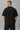 Back view of a man wearing a black HORN OK PLEASE oversized t-shirt with gold 'POPCASE' logo on the upper back.