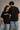 A couple wearing matching black oversized Hot Wheels t-shirts and light wash jeans, posing intimately against a neutral background.