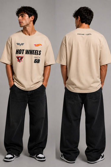 Man wearing a black STAR BOY oversized t-shirt with "Hot Wheels" graphics, sitting on a black couch. Streetwear fashion. - beige