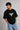Person wearing a black t-shirt with a white logo on a plain background