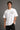 Man wearing a white RAM YODHA oversized t-shirt with 'Ram' graphic on front and Ram Yoddha artwork on back, seated on wooden steps. - white