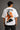 Man wearing a white RAM YODHA oversized t-shirt with 'Ram' graphic on front and Ram Yoddha artwork on back, seated on wooden steps.