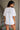 Woman wearing a white t-shirt with text on the back, standing in a neutral indoor setting.