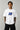 Man wearing a white VIRAT MCG 18 Vs PAK oversized t-shirt with a blue galaxy-themed '18' graphic. He is sitting on steps, showcasing the relaxed fit and streetwear style.