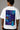 Man wearing a white VIRAT MCG 18 Vs PAK oversized t-shirt with a blue galaxy-themed '18' graphic. He is sitting on steps, showcasing the relaxed fit and streetwear style.