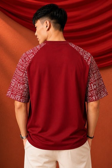 Dark red POPCASE 'Unstoppable' oversized t-shirt with white raised print, featuring ethnic patterned sleeves. Close-up shot showcasing fabric texture and print detail.