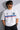 Man wearing a white BMW oversized t-shirt with blue, light blue, and red stripes across the chest and a black Puma logo and BMW M Motorsport emblem.