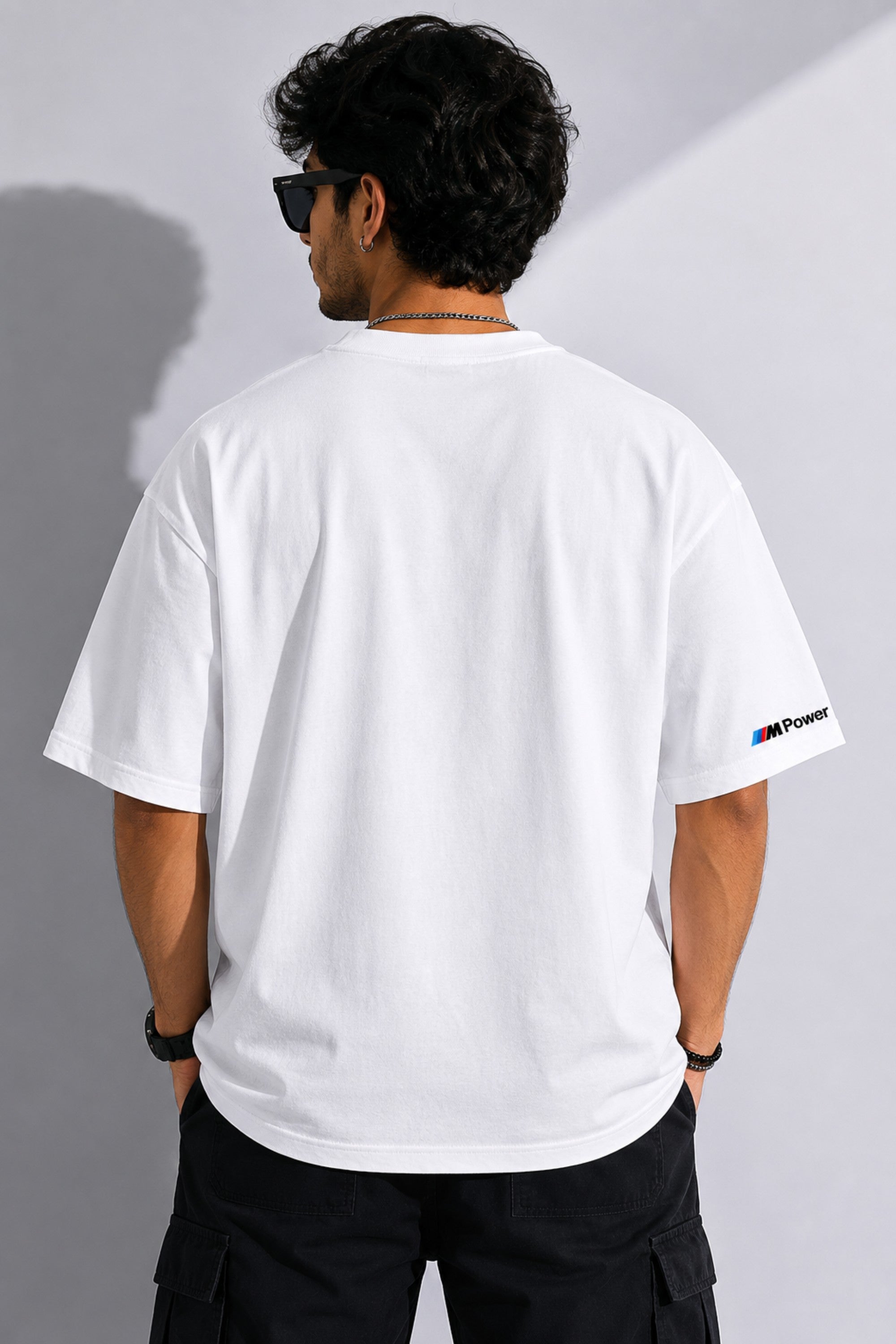 Man wearing a white BMW oversized t-shirt with blue, light blue, and red stripes across the chest and a black Puma logo and BMW M Motorsport emblem.