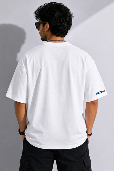 Man wearing a white BMW oversized t-shirt with blue, light blue, and red stripes across the chest and a black Puma logo and BMW M Motorsport emblem.