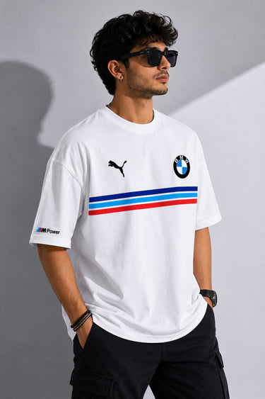 Man wearing a white BMW oversized t-shirt with blue, light blue, and red stripes across the chest and a black Puma logo and BMW M Motorsport emblem.