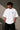 Man wearing a white oversized BMW M "530i E60" graphic t-shirt and black baggy jeans, standing against a textured concrete wall.