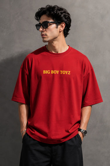 Red BIG BOY TOYZ x Hot Wheels oversized t-shirt featuring a vintage red Hot Wheels car graphic, checkered flag pattern, and brand logos. Showcase print quality and fabric.