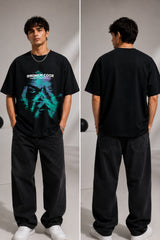 Man wearing a black BROKEN CODE oversized t-shirt with a glitch art graphic of eyes and text. Features a chain necklace and dark wash jeans. Model is posed against a studio backdrop.