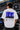 Model wearing white POPCASE Carlos Sainz Williams Racing oversized t shirt with blue W logo at Formula 1 circuit pitlane