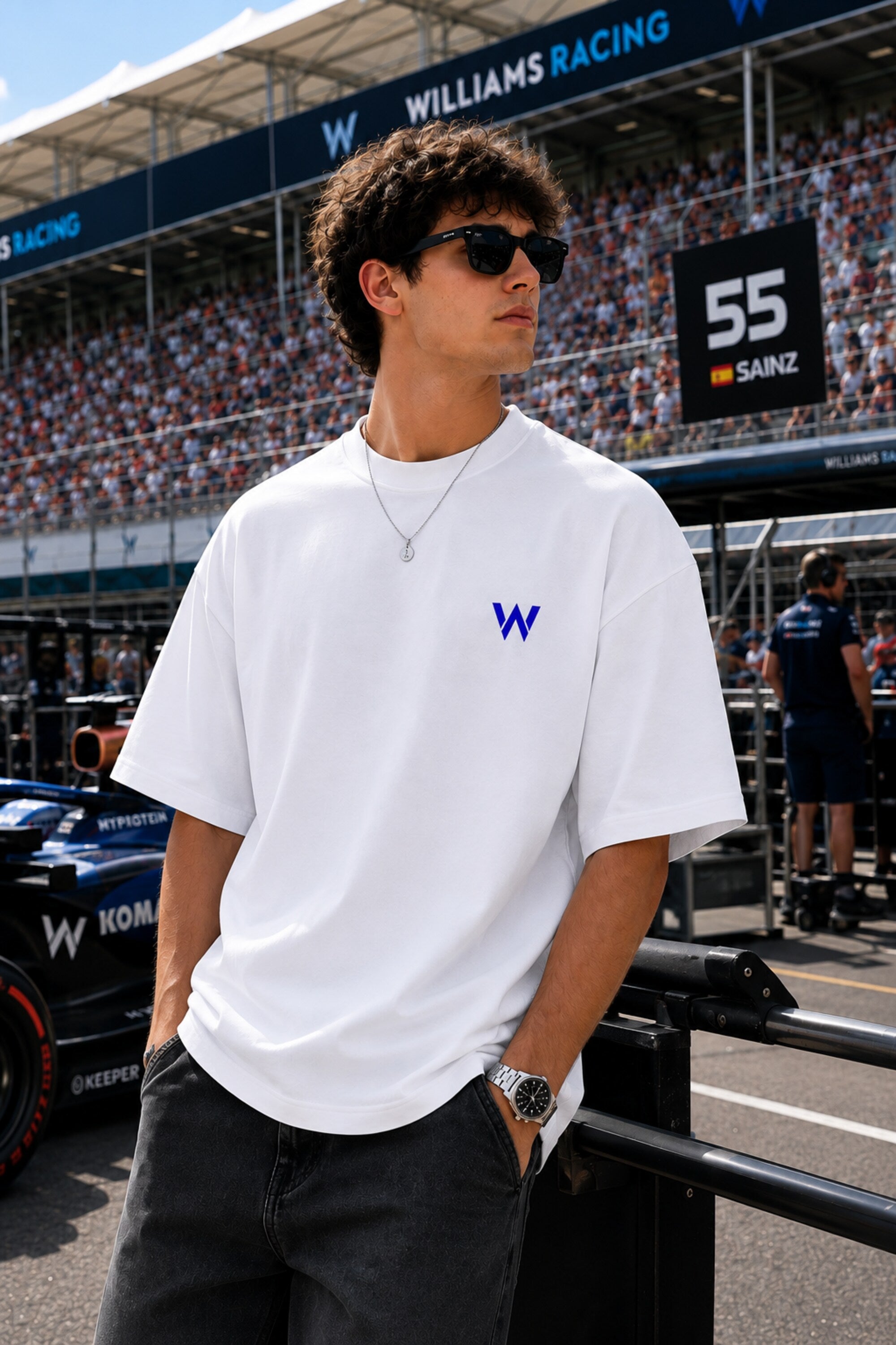 Model wearing white POPCASE Carlos Sainz Williams Racing oversized t shirt with blue W logo at Formula 1 circuit pitlane