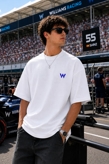 Model wearing white POPCASE Carlos Sainz Williams Racing oversized t shirt with blue W logo at Formula 1 circuit pitlane