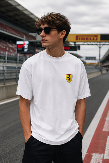 Model wearing white POPCASE Charles Leclerc Scuderia Ferrari oversized t shirt with prancing horse shield badge at F1 circuit pitlane