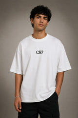 Man wearing a white CR7 oversized t-shirt with black CR7 logo. Studio shot with grey background.
