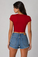 Model wearing a red CROPTOP Cherry crop top with a cute cherry and bow graphic, paired with denim shorts. The top has a flattering cropped fit.