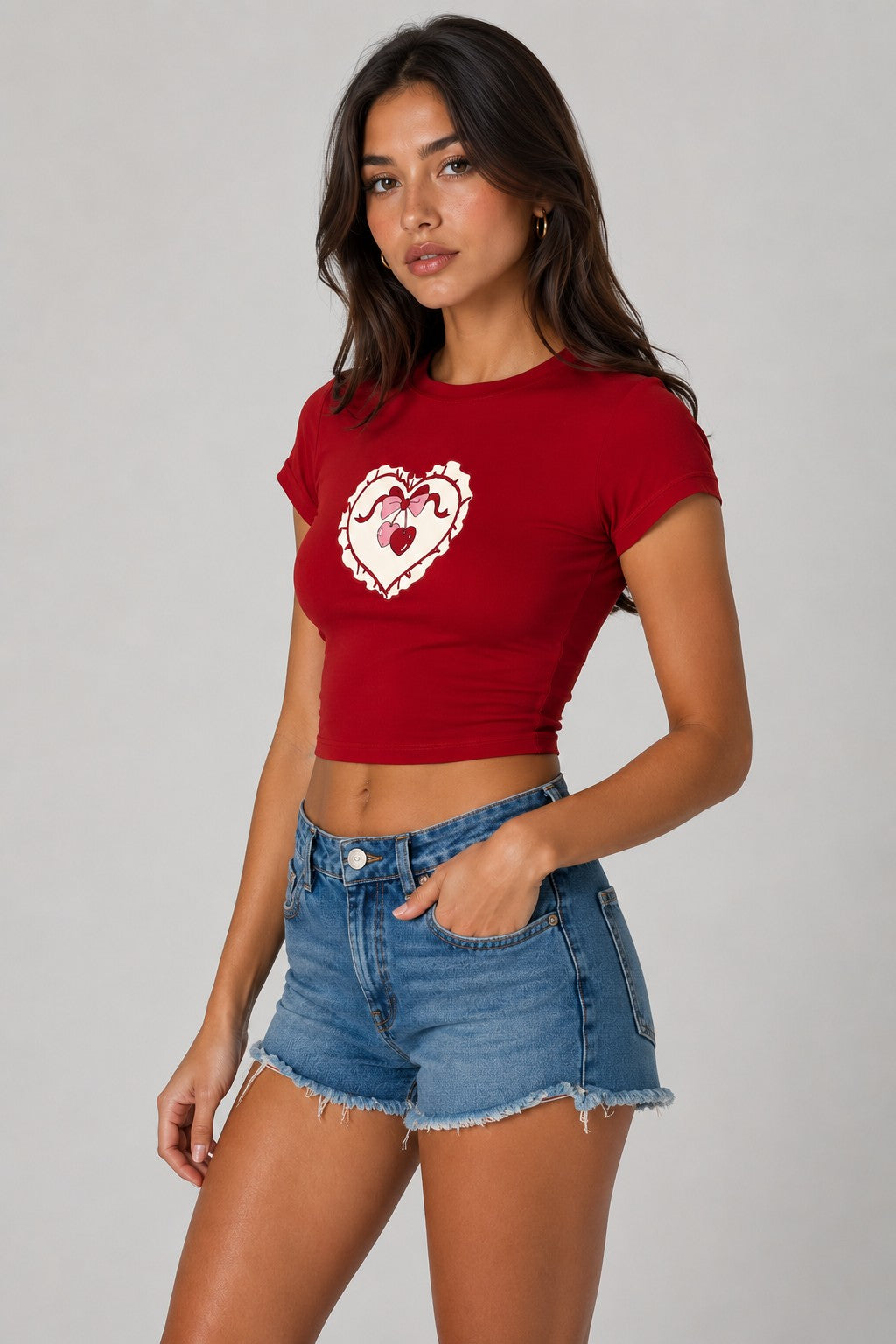 Model wearing a red CROPTOP Cherry crop top with a cute cherry and bow graphic, paired with denim shorts. The top has a flattering cropped fit.