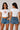 Model wearing a red CROPTOP Cherry crop top with a cute cherry and bow graphic, paired with denim shorts. The top has a flattering cropped fit. - white