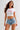 Woman wearing a white crop top with red trim and "New York" graphic, paired with denim shorts, sitting on a textured armchair.