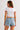 Woman in white ringer crop top with red trim and 'New York' graphic, paired with denim shorts, sitting on a couch.