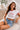 Woman wearing a white crop top with red trim and "New York" graphic, paired with denim shorts, sitting on a textured armchair.