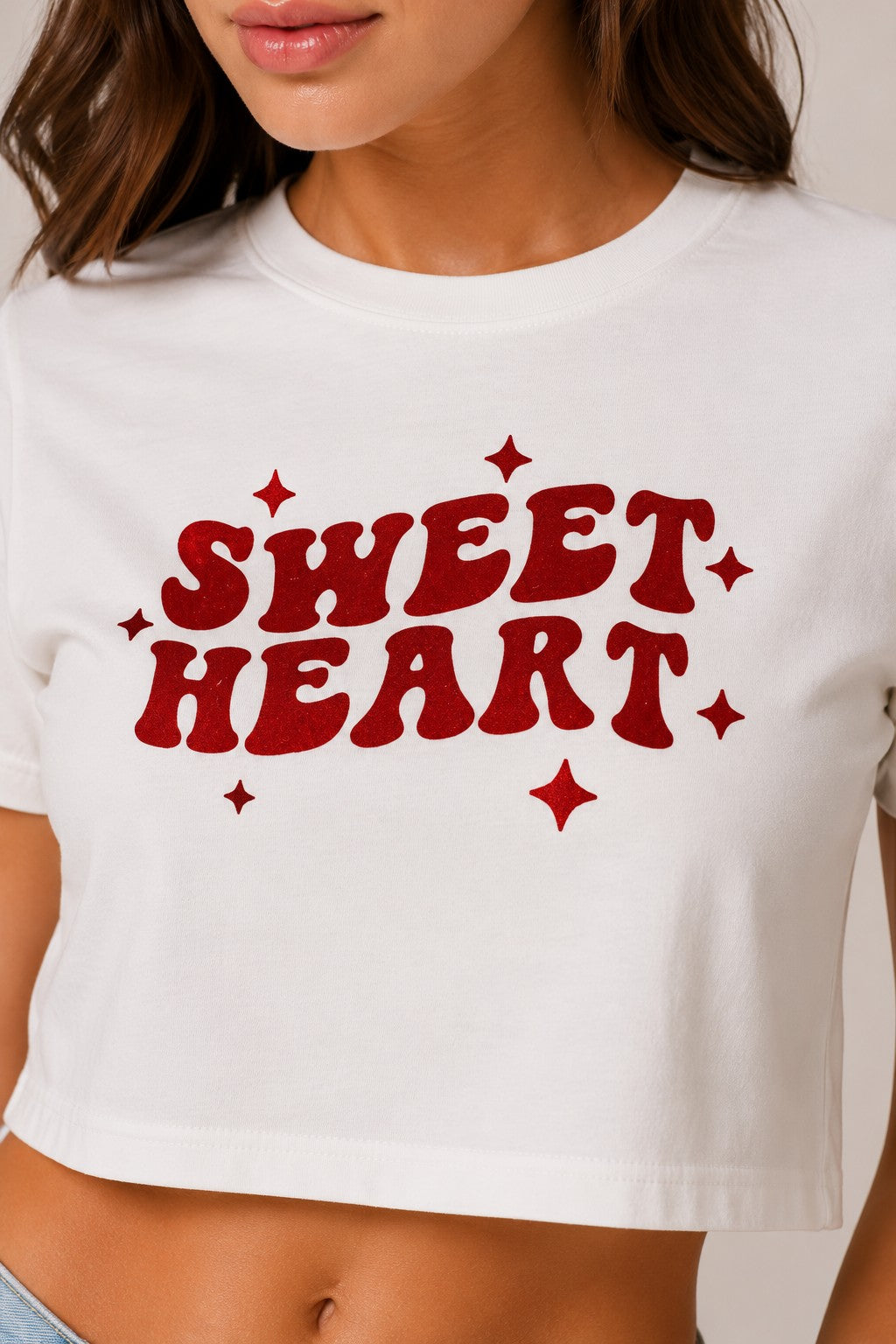 Model wearing a white "Sweet Heart" graphic oversized croptop t-shirt with red distressed lettering and star accents. Streetwear fashion.